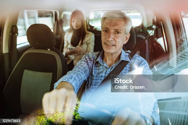 Businesswoman Using Taxi Ride To Go To Work Gray Hair Taxi Driver With Seat Belt On Stock Photo - Download Image Now
