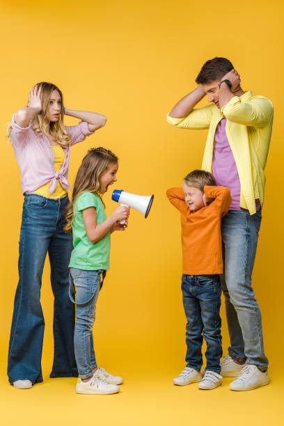 istock daughter yelling into megaphone on brother while parents closing ears on yellow 1221478631
