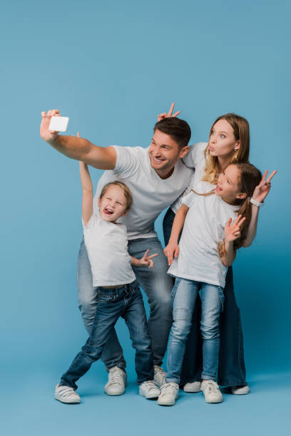 istock cheerful family showing victory signs while taking selfie on smartphone on blue 1221478659