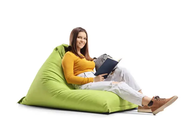 Photo of Young woman sitting on a green beanbag with a book and smiling at the camera