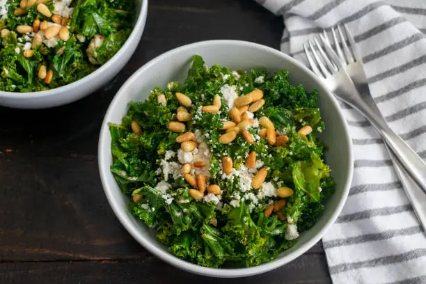 Kale salad with sweet onion dressing topped with crumbled goat cheese and toasted pine nuts