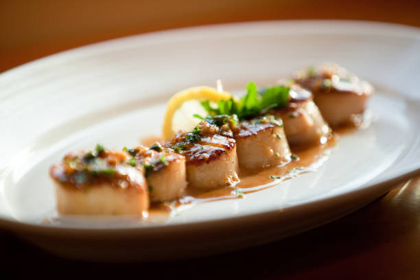 istock Scallops with Sauce in a Row with Garnish and Lemon Wedge - Gourmet Dinner 1221483525