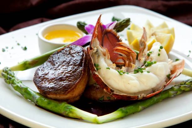 Bacon Wrapped Filet Mignon and Lobster Tail with Asparagus, Melted Butter, and Lemon Wedge - Gourmet Dinner Plate stock photo