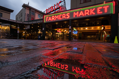 Seattle, USA - Apr 22, 2020: Deserted Pike Place Market illuminated with reflections in a puddle early in the night at the height of the Coronavirus Stay at home order.