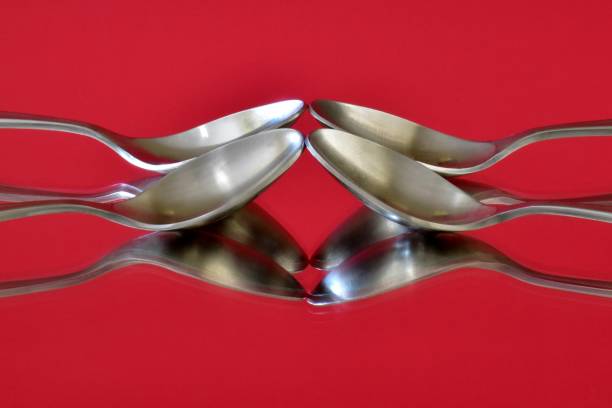 Four spoons arranged and photographed on a vivid pink mirrored surface.