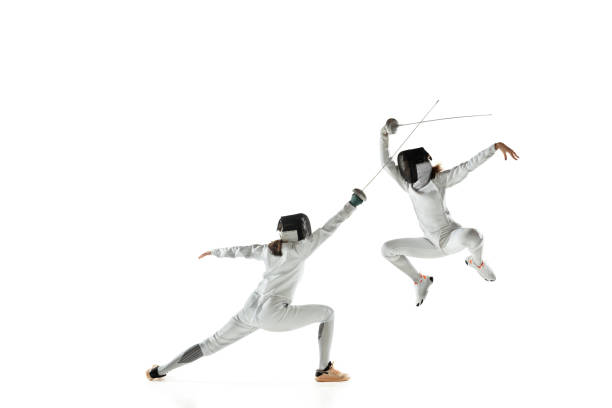 Teen girls in fencing costumes with swords in hands isolated on white background Teen girls in fencing costumes with swords in hands isolated on white studio background. Young female models practicing and training in motion, action. Copyspace. Sport, youth, healthy lifestyle. face guard sport stock pictures, royalty-free photos & images