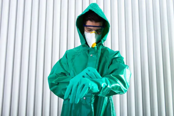 Specialist standing indoors in hazmat suit and putting on his sterile rubber gloves stock photo