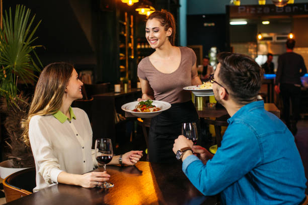 レストランで若いカップルにサービスを提供する若いウェイトレス - restaurant dinner waitress dining ストックフォトと画像