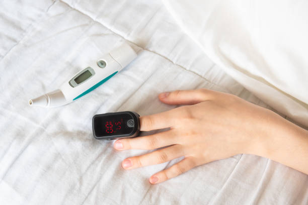 close-up of woman's hand wearing pulse oxymeter on finger with digital thermometer on bed - taking pulse oximeter medical oxygen equipment human lung imagens e fotografias de stock