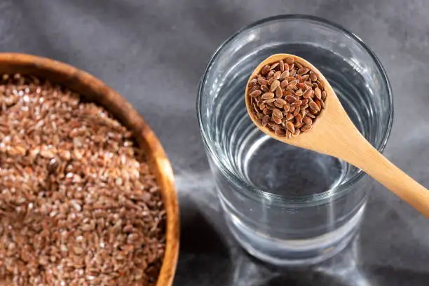 Linum usitatissimum - Spoon with organic flaxseeds and glass of filtered water