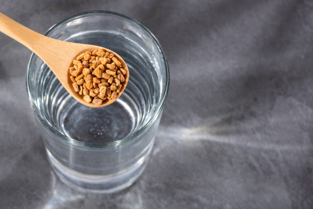 Trigonella foenum-graecum - Spoon with fenugreek seeds and glass of filtered water Spoon with fenugreek grains to mix with water - Trigonella foenum-graecum fenugreek stock pictures, royalty-free photos & images