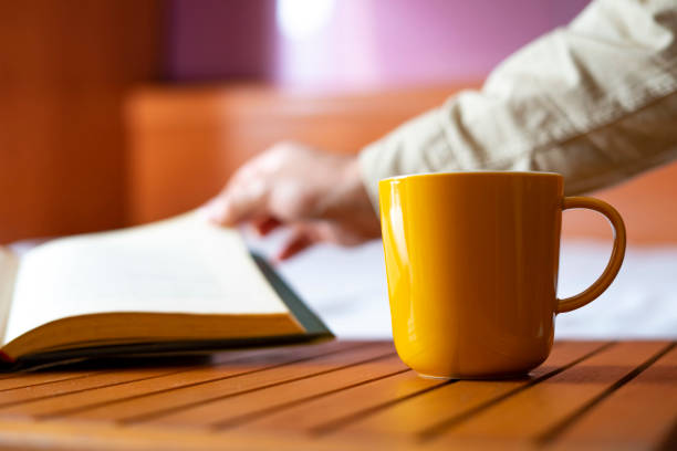 Yellow cup of coffee and a man turning a page in a book.