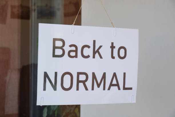 istock 'Back to normal' sign hanging from a store window after Coronavirus (Covid-19) lockdown measures are being eased off. Economy restart concept. 1221498794