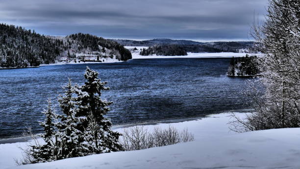 istock River that thaws in spring lined with snow-covered trees under overcast skies 1221499781