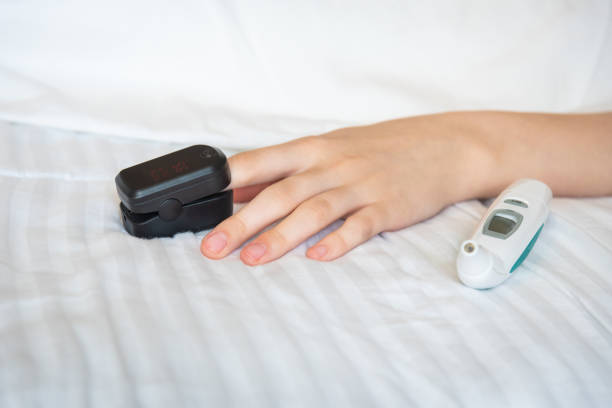 woman's hand resting on bed with digital thermometer and wearing pulse oxymeter on finger - taking pulse oximeter medical oxygen equipment human lung imagens e fotografias de stock