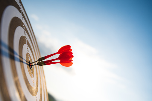 Close up shot red darts arrows in the target center on dark blue sky background. Business target or goal success and winner concept.