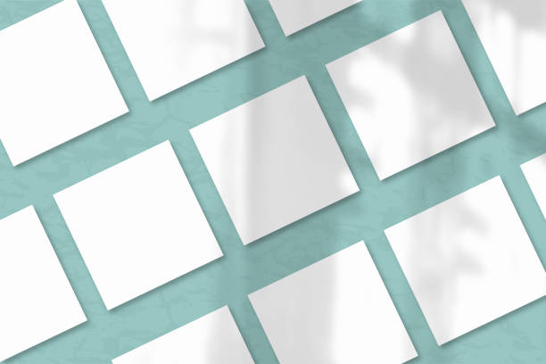 istock Several square sheets of white textured paper against a blue-green wall. Natural light casts shadows from the window. Flat lay, top view 1221506936