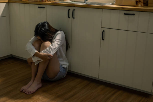 joven deprimida hermosa mujer asiática sentada en el suelo de la cocina con las rodillas abrazadas. soledad triste adolescente que vive sola en casa y llora. concepto de salud mental, abuso de drogas y cuestión social. - abrazar las rodillas fotografías e imágenes de stock