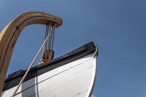 Vintage wooden lifeboat attached to a hoist, against a brilliant blue sky, horizontal aspect