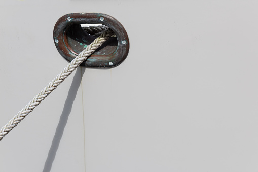 Patina on metal hawsehole in a white boat hull with white rope, clean marine copy space, horizontal aspect