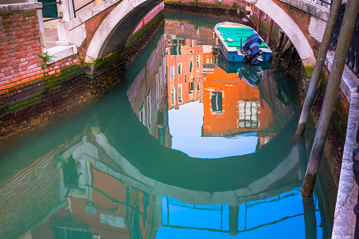 Venetian boat on water Canal under bridge reflection at sunrise - Venice, Italy