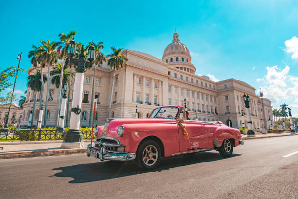 Old classic American pink car rides in front of the Capitol. November 26, 2019, Havana, Cuba: Old classic American pink car rides in front of the Capitol. Retro convertibles are used as taxis to transport tourists in Cuba. cuba stock pictures, royalty-free photos & images