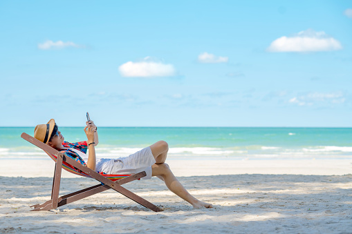 Young Asian man lying on beach chair with using smartphone on the beach