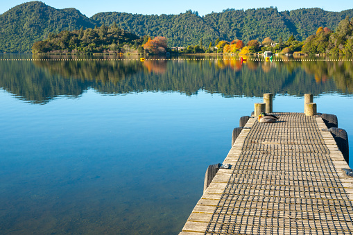 lake Tarawera view from jetty across lake to autumn colors and surrounding tree clad hills.