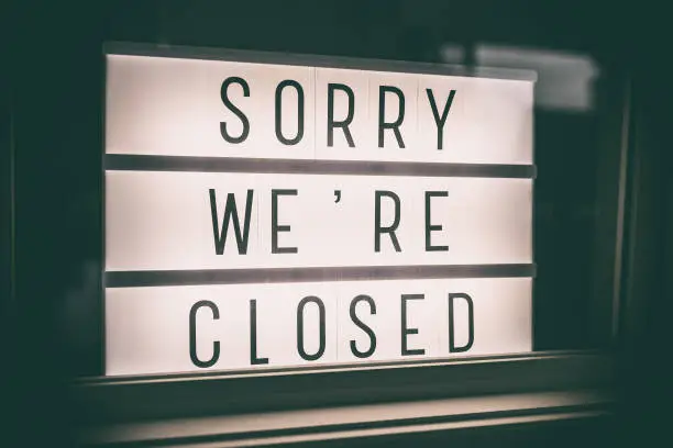 SORRY WE'RE CLOSED storefront window sign. Coronavirus Closure due to COVID-19 message board in business retail store lightbox at night. Shutdown of restaurants, stores, non essential services.