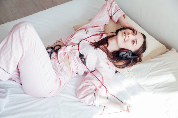 femme brune dans des pyjamas roses écoutant la musique avec des écouteurs - brightly lit audio photos et images de collection
