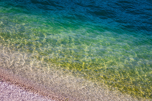 Detail of translucent and idyllic lake Garda shore, turquoise water surface in Malcesine