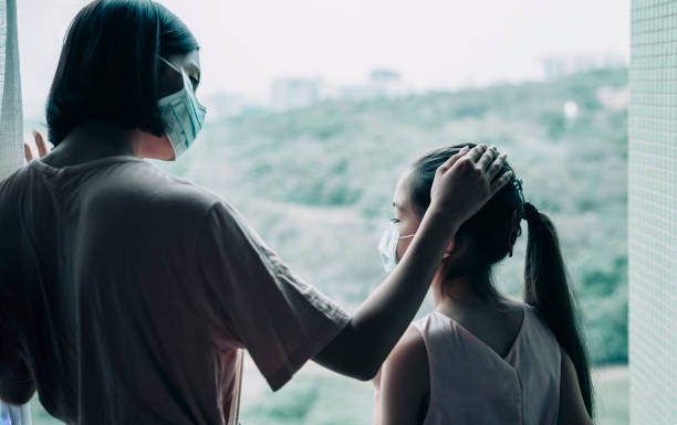 istock Mother with daughter child in mask looking from window 1221537094