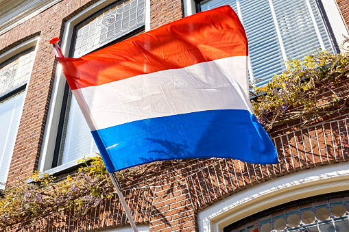 Dutch flag waving in the wind on the facade of a typical dutch house on Koningsdag. A national holiday in the Kingdom of the Netherlands.