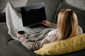 Beautiful young woman relaxing on comfortable couch and using laptop at home.