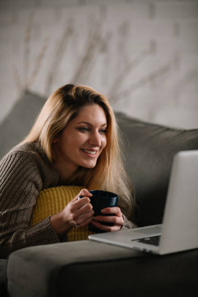 istock Beautiful young woman relaxing on comfortable couch and using laptop at home. 1221537806