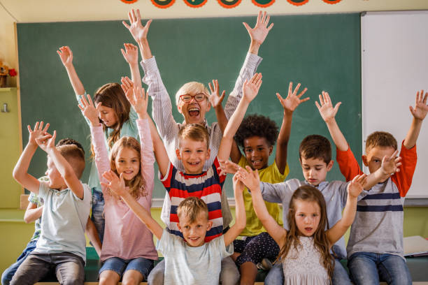 istock Happy teacher and elementary students with raised arms in the classroom. 1221539990