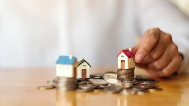 Photo of a woman's hand putting house model on pile of coins for saving money concept
