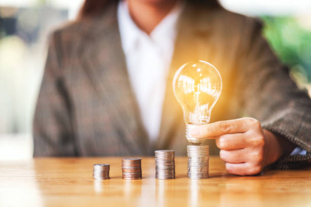 istock Businesswoman holding and putting light bulb on coins stack on the table 1221541618