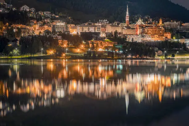 St Moritz illuminated at night and reflection on peaceful lake, Engadine – Switzerland