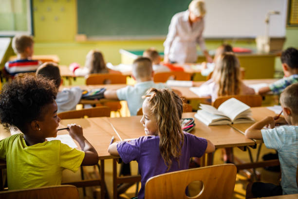 istock Rear view of smiling schoolgirls talking during a class at elementary school. 1221541901