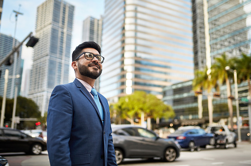 Low angle view of successful Miami businessman in mid 30s wearing suit and looking up with a smile as he stands outdoors in downtown district.