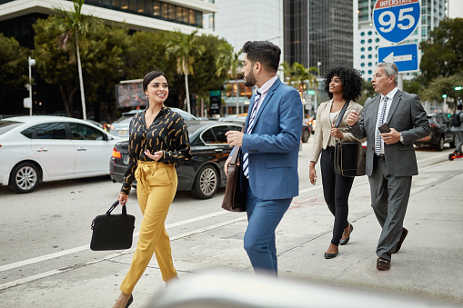 Male and female Hispanic and African-American business colleagues in 20s, 30s, and 60s walking side by side in downtown Miami and sharing ideas.