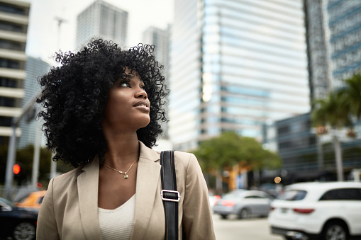 Front view of 21 year old African-American female corporate professional looking up and away from camera with optimistic expression in downtown Miami.