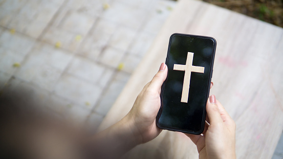 Woman's hand with cross in screen mobile phone. Concept of hope, faith, christianity, religion, church online.