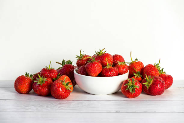 istock Fresh strawberries in white ceramic bowl on white wooden table 1221548786