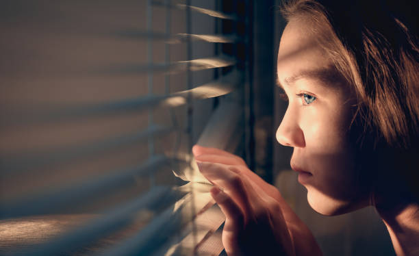 a garota olha pela janela empurrando as cortinas com as mãos. conceito de quarentena. - eastern european flash - fotografias e filmes do acervo