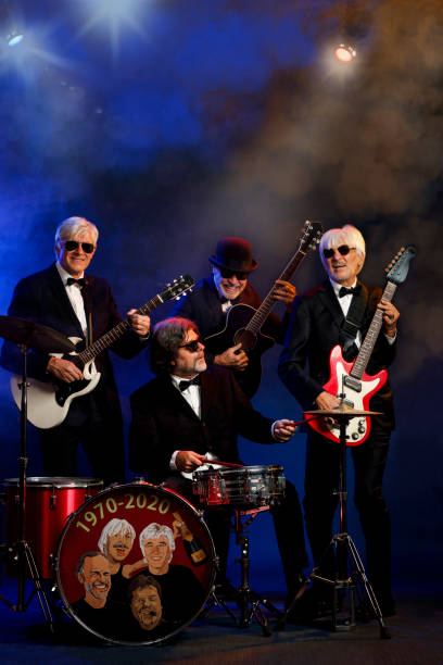 istock Musician group guitarist and drummer Active senior Handsome man playing guitar and drum. Best friends. Blue  background, with rays of light and special effects smoke. 1221551384