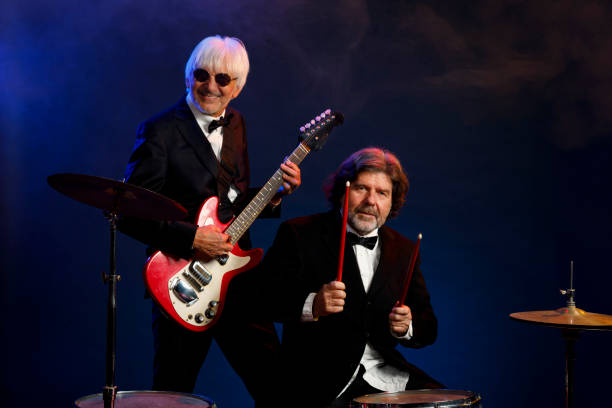 istock Musician group guitarist and drummer Active senior Handsome man playing guitar and drum. Best friends. Blue  background, with rays of light and special effects smoke. 1221551409