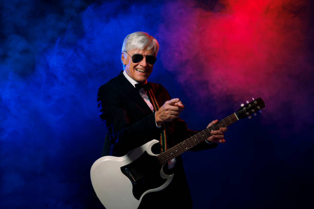 istock Musician Guitarist Active senior Handsome man playing guitar. Blue  background, with rays of light and special effects smoke. 1221551956