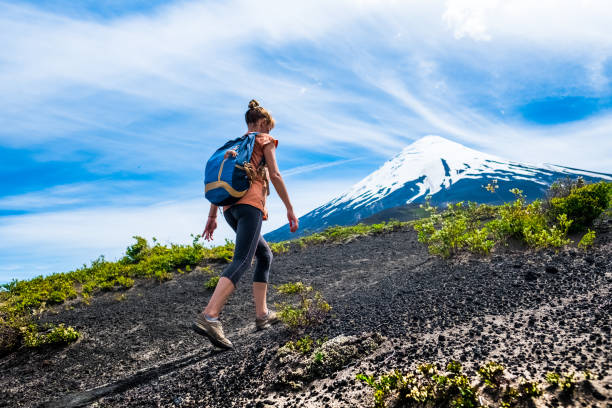 młoda kobieta spacerowicz spacery na luźnym skalistym szlaku z wulkanu ośnieżone na tle. trekking do wulkanu osorno w chile - snow capped mountain peaks zdjęcia i obrazy z banku zdjęć